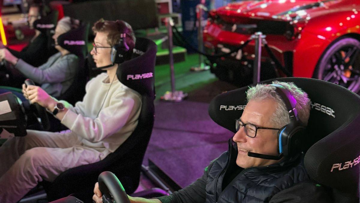 Zwei Generationen fahren nebeneinander in Rennsimulatoren, im Hintergrund ein roter Ferrari — Sim Racing für die ganze Familie