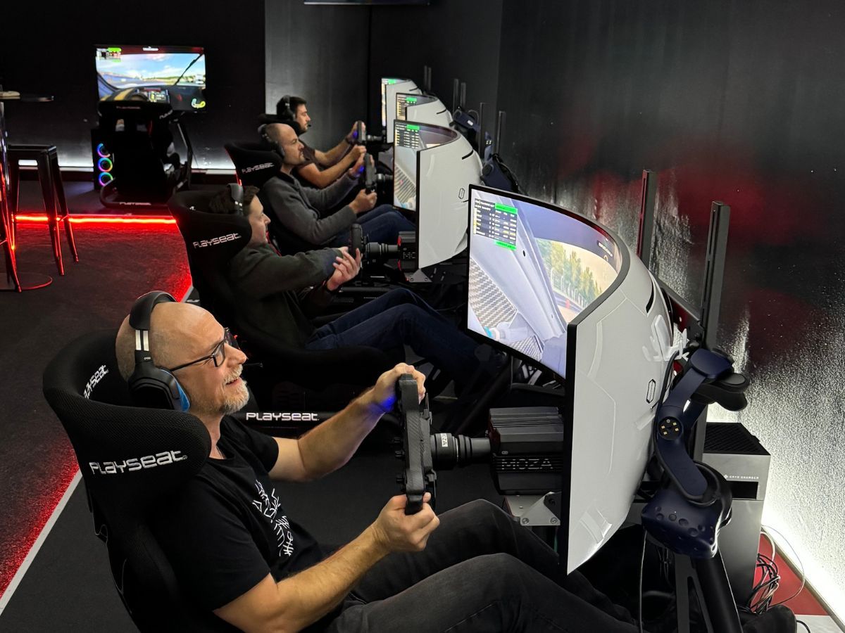 Firmenteam beim Sim-Racing-Event, mehrere Mitarbeitende fahren nebeneinander an Rennsimulatoren