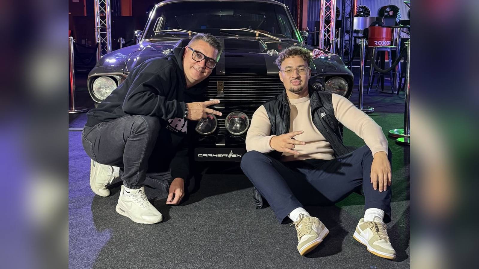 Paddock Talk: die beiden Hosts vor einem Muscle Car im AP Café Indoor-Racing