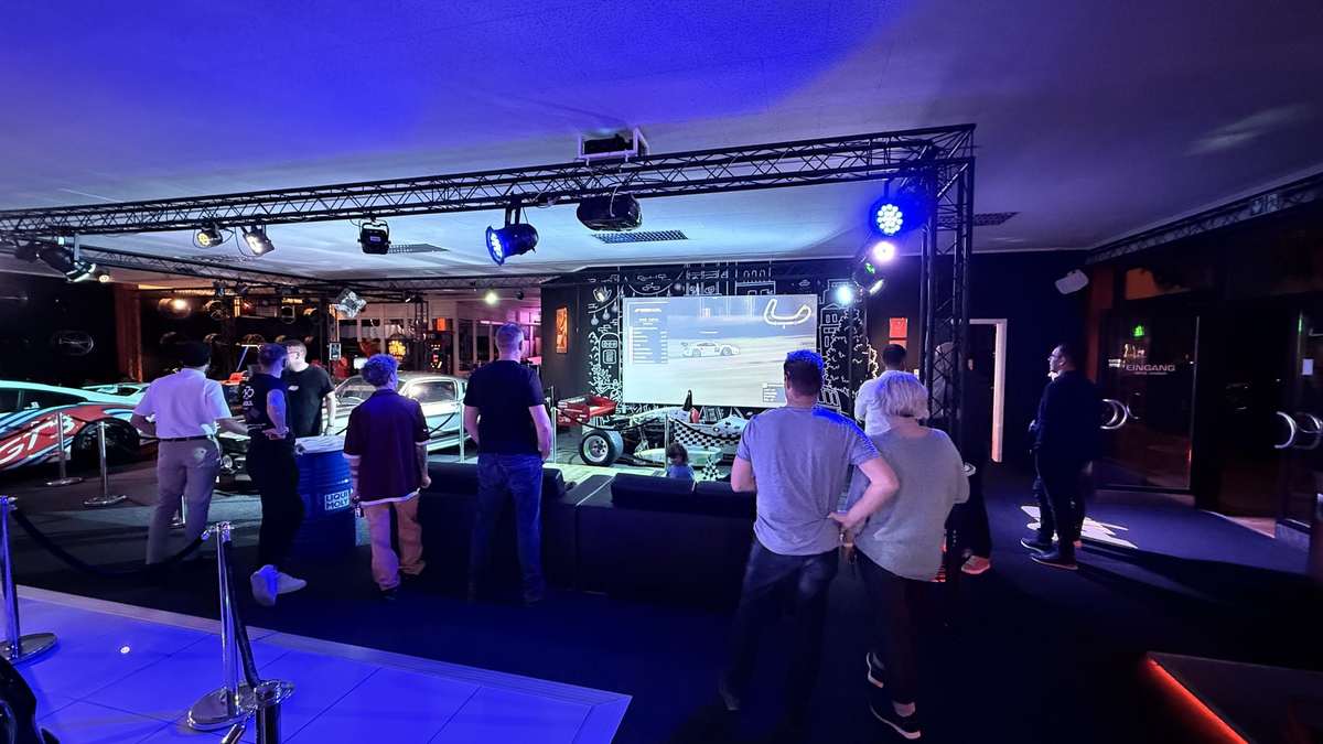 Public Viewing im Sim Racing Center Aadorf: Gäste verfolgen das Rennen auf der grossen Leinwand, daneben Sport- und Rennwagen der Auto-Ausstellung