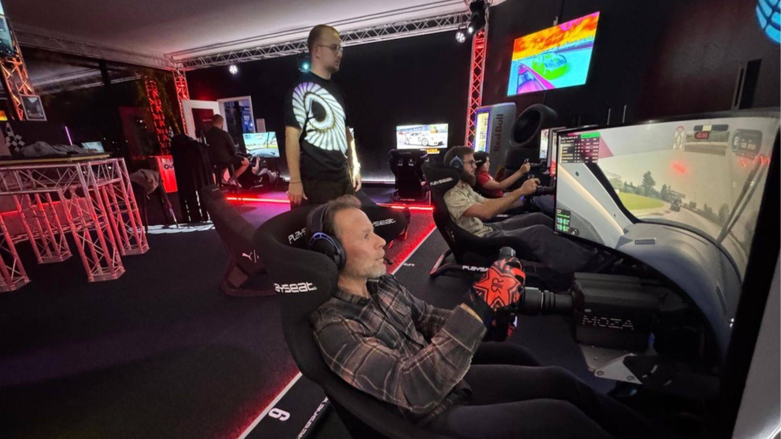 Race-Club-Abend im Sim Racing Center Aadorf: Mitglieder sitzen in Rennsimulatoren und fahren ein Rennen, daneben Monitore mit Live-Rennbild und rote Traversen-Beleuchtung
