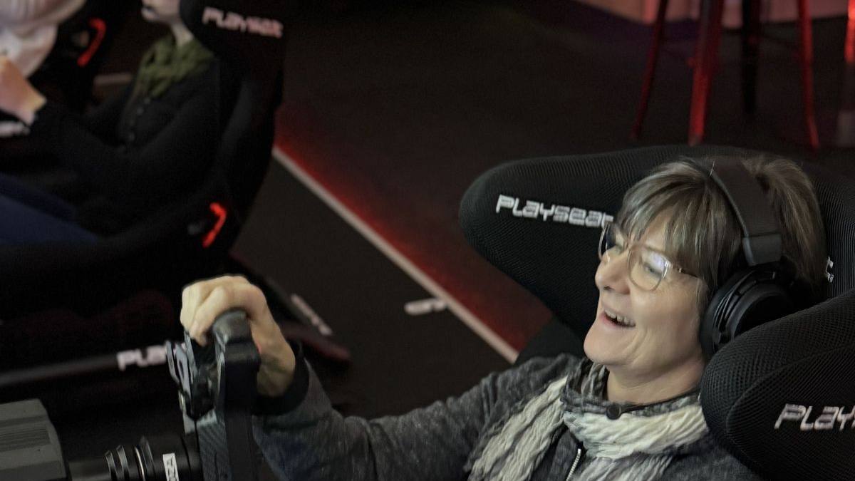 Frau 50+ lacht begeistert am Lenkrad eines Rennsimulators beim Sim Racing