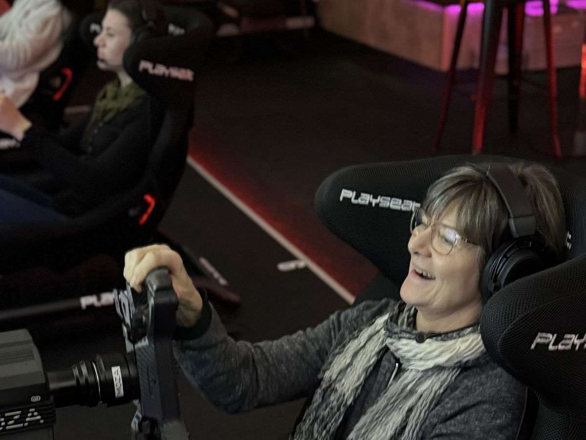 Frau 50+ lacht begeistert am Lenkrad eines Rennsimulators beim Sim Racing