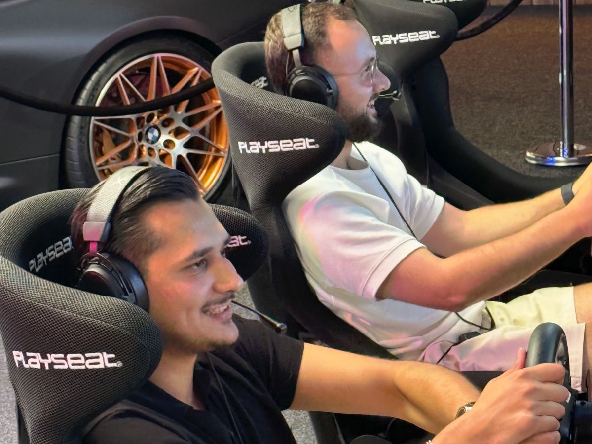 Zwei Freunde lachen beim Sim Racing an den Rennsimulatoren, im Hintergrund ein BMW