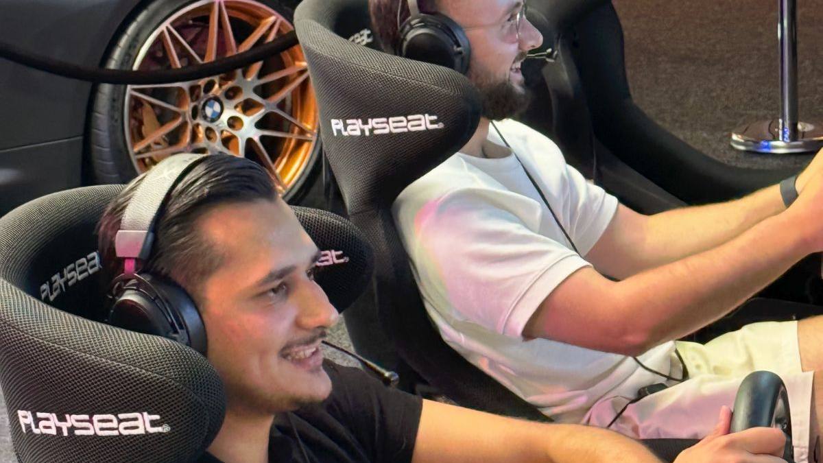 Zwei Freunde lachen beim Sim Racing an den Rennsimulatoren, im Hintergrund ein BMW