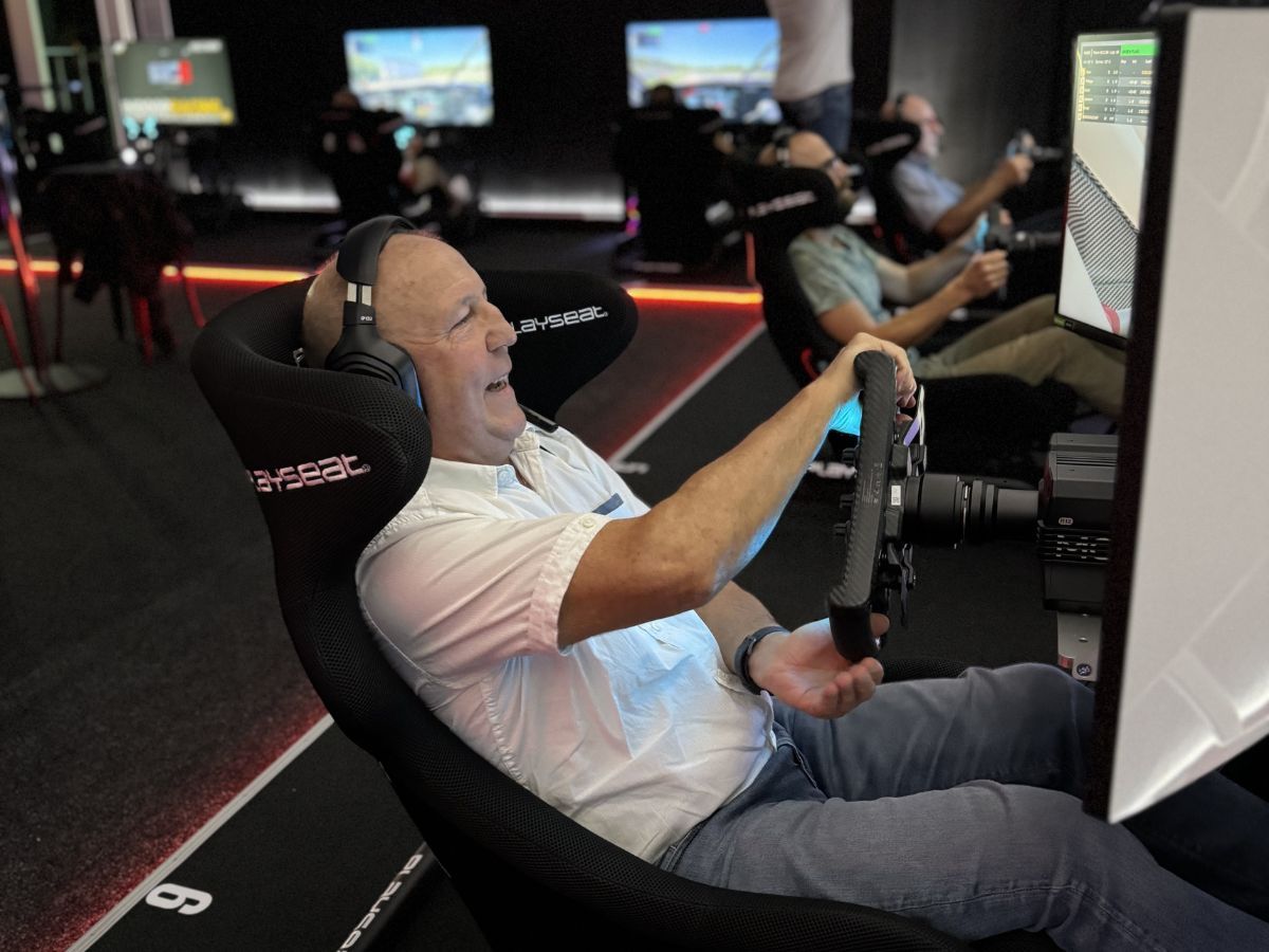 Älterer Fahrer mit Headset lacht am Lenkrad eines Rennsimulators — Sim Racing ohne Altersbegrenzung