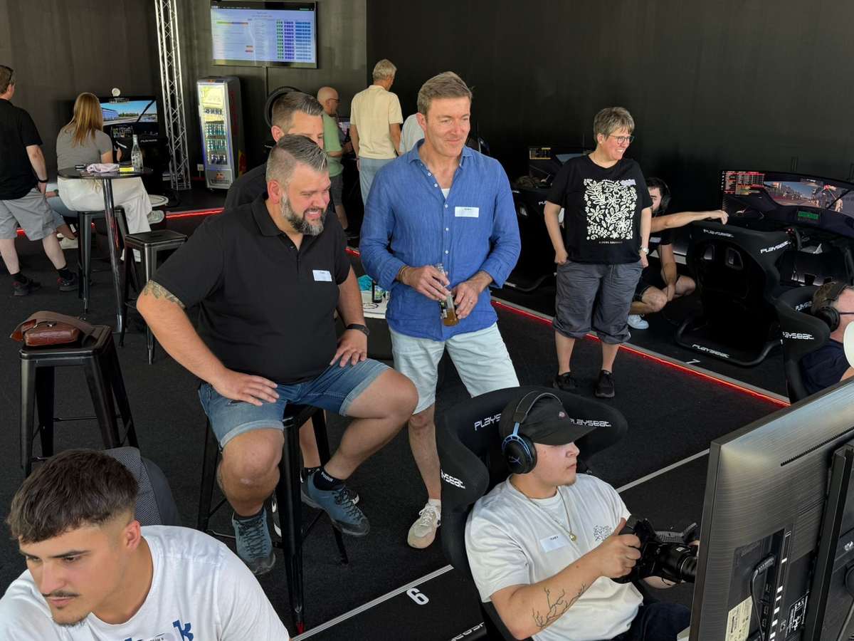 Firmen-Team-Event im Sim Racing Center Aadorf: Teilnehmende mit Namensschildern rund um die Playseat-Rennsimulatoren, ein Fahrer mit Headset am Lenkrad vor dem gebogenen Bildschirm, im Hintergrund die Anzeigetafel mit den Rundenzeiten