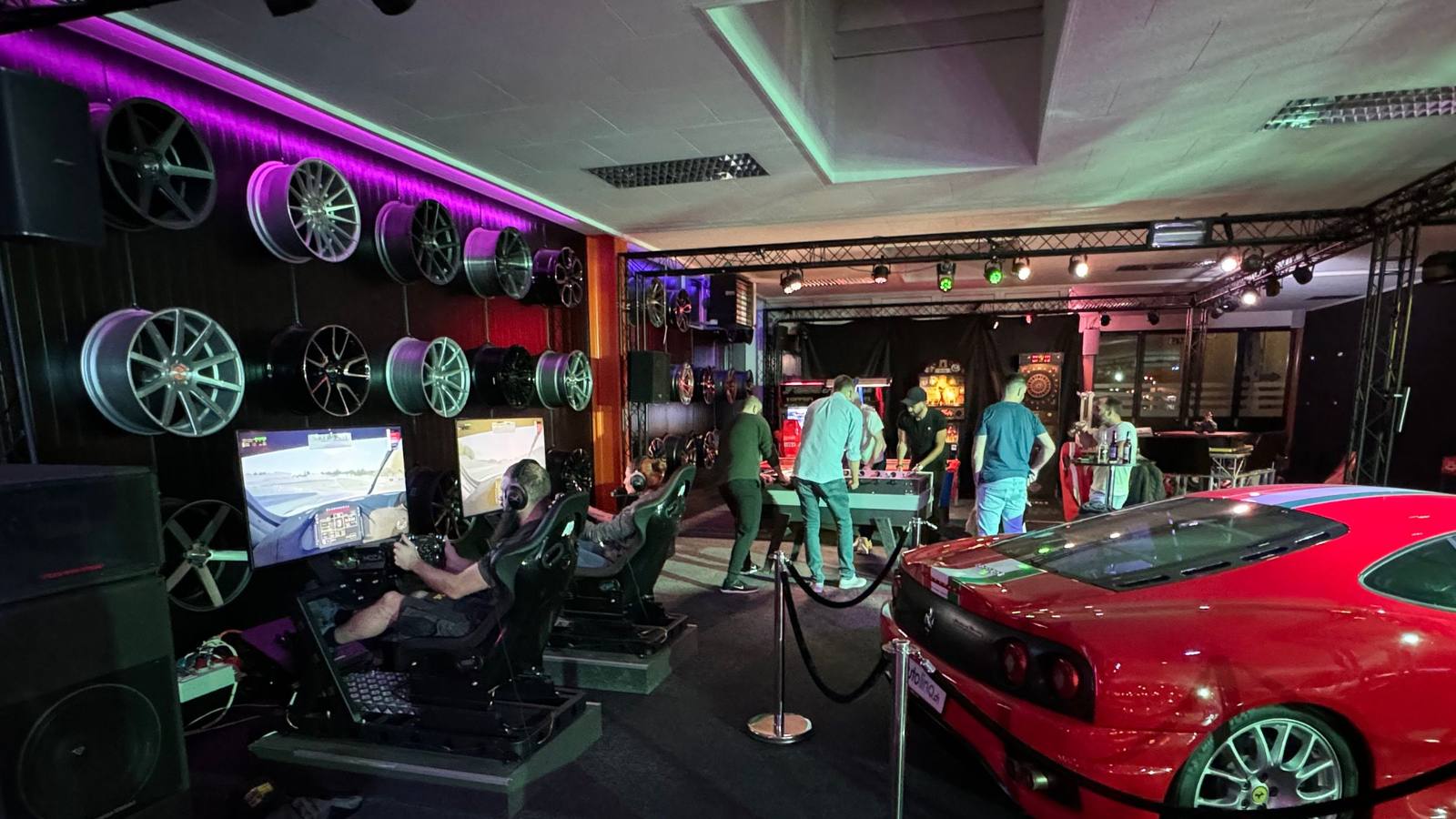 Zwei Fahrer an den Rennsimulatoren vor der Felgenwand, dahinter Töggelikasten und der rote Ferrari der Ausstellung im Sim Racing Center Aadorf — Team-Event einer Firma aus Schaffhausen