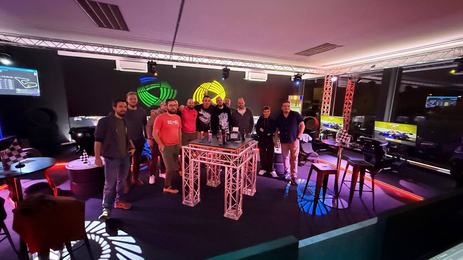 Firmenteam beim Apéro an den Stehtischen unter den leuchtenden Indoor-Racing-Logos im Sim Racing Center Aadorf — Team-Event einer Firma aus St. Gallen
