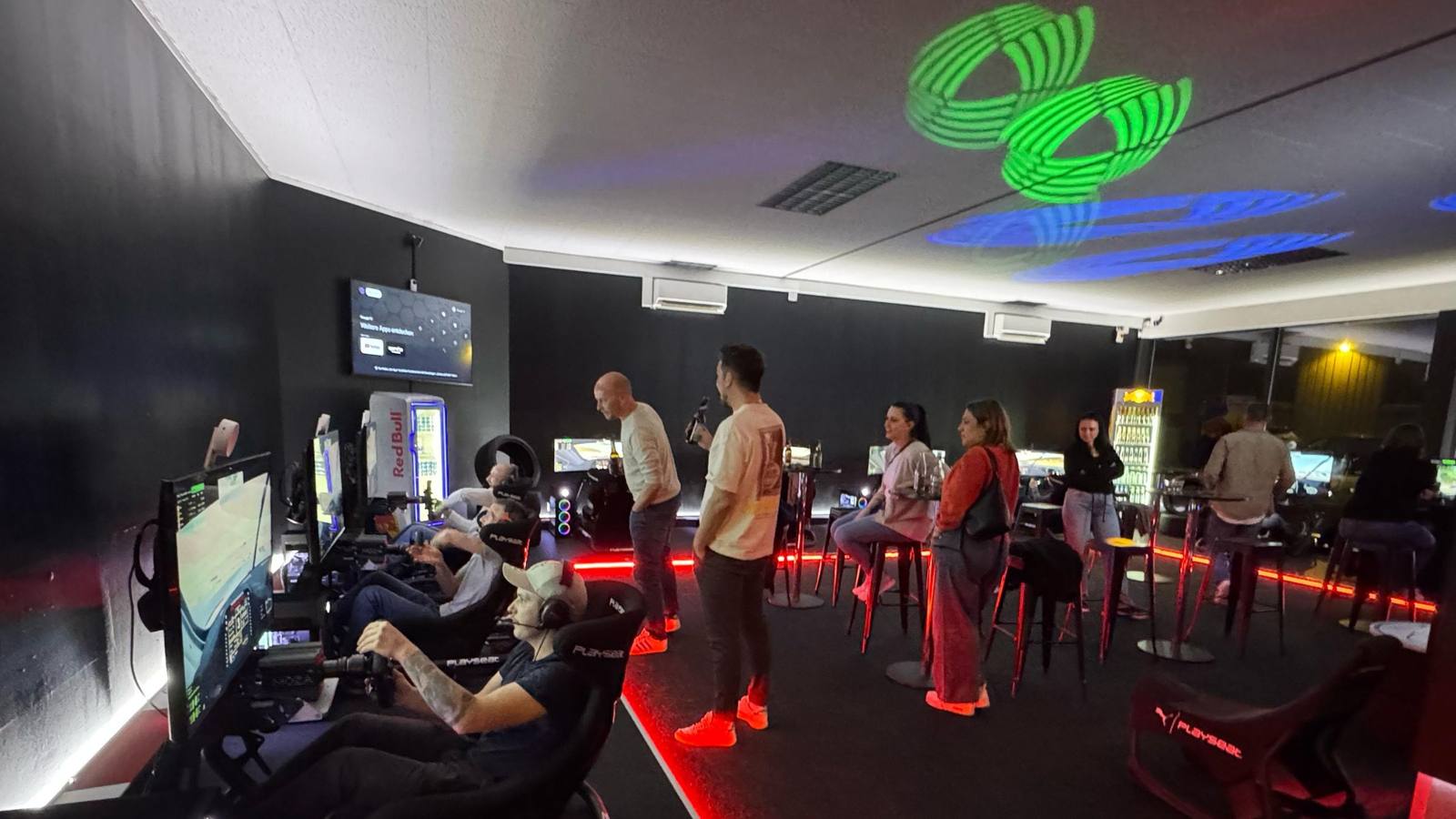 Fahrerinnen und Fahrer in den Rennsimulatoren, das übrige Team schaut von den Stehtischen zu — Team-Event einer Firma aus Zürich im Sim Racing Center Aadorf