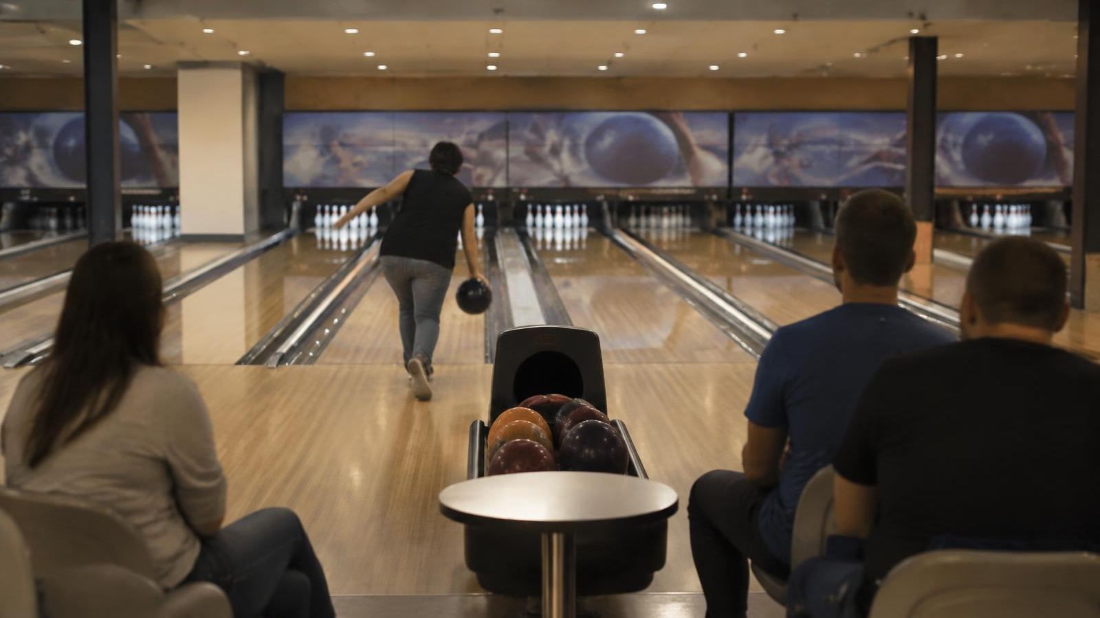 Bowlingbahn, eine Person wirft, die übrigen warten auf der Bank (KI-Symbolbild)